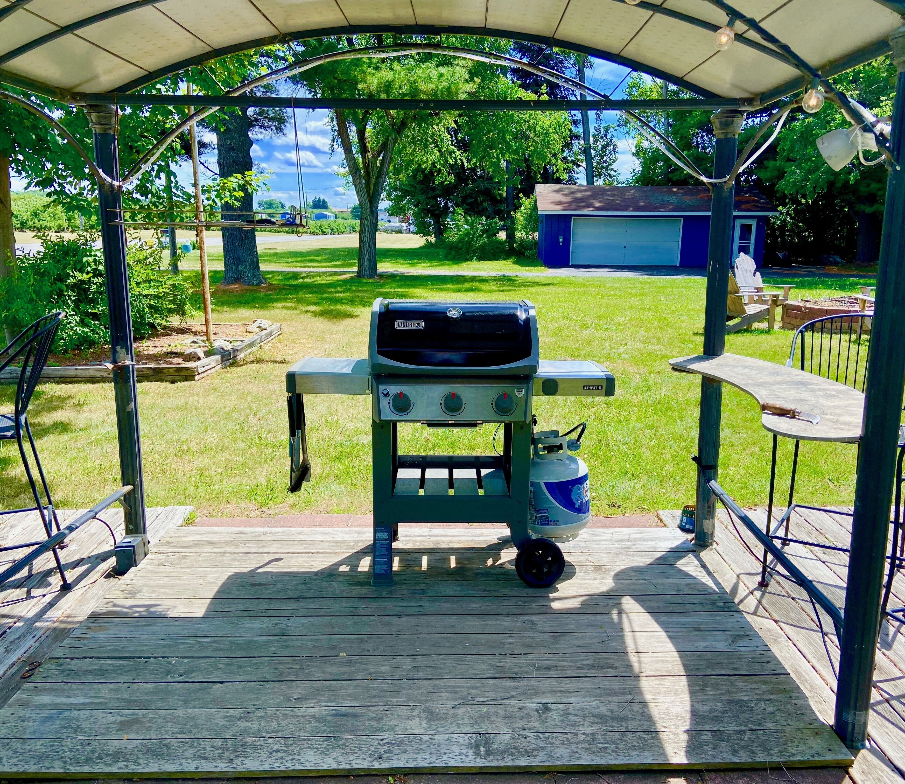A covered outdoor barbecue area with a grill, a propane tank, and a table with chairs.