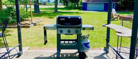 A covered outdoor barbecue area with a grill, a propane tank, and a table with chairs.