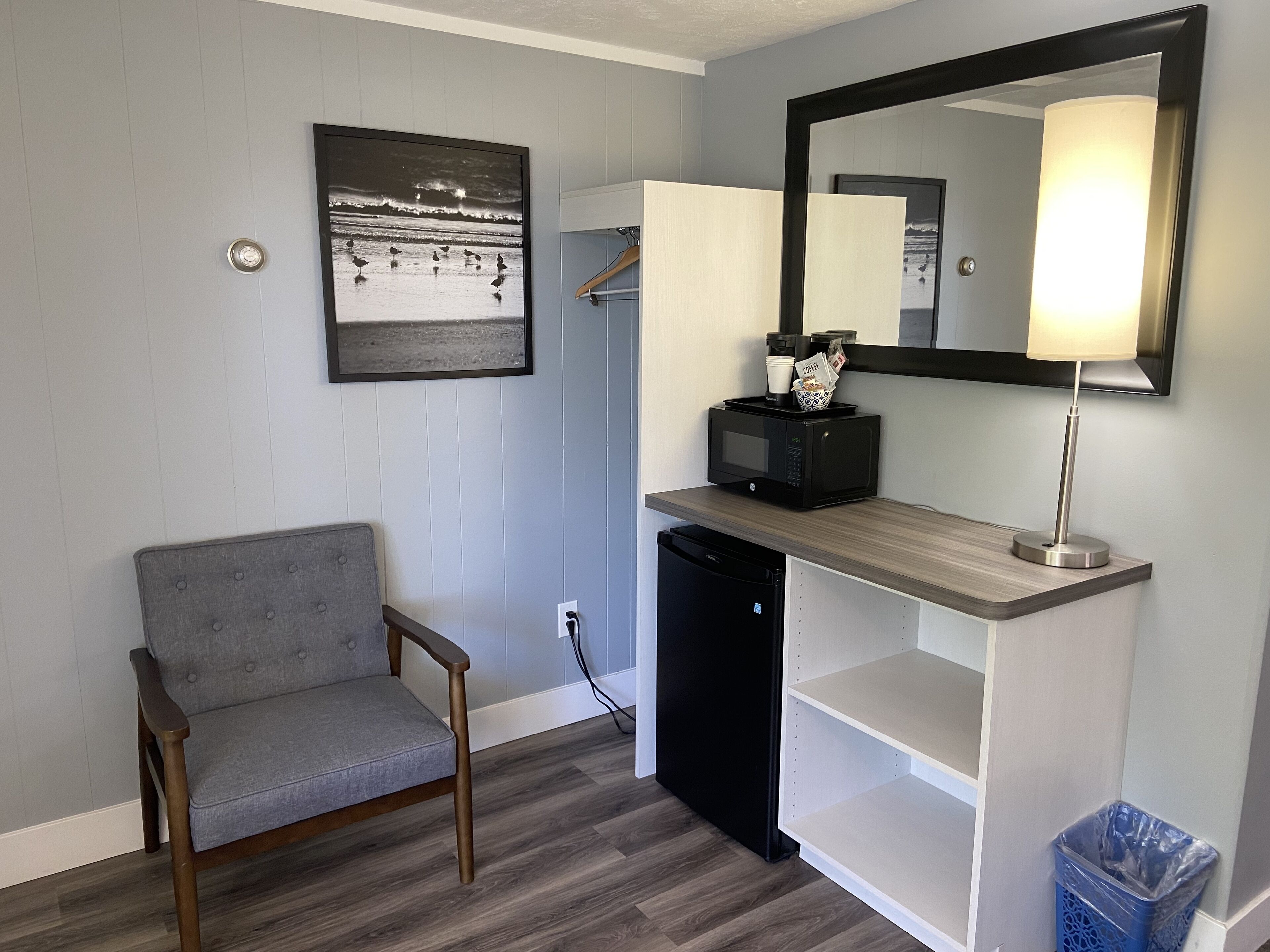 A compact room with a grey sofa, a black refrigerator, a microwave, a small shelf, and a mirror.