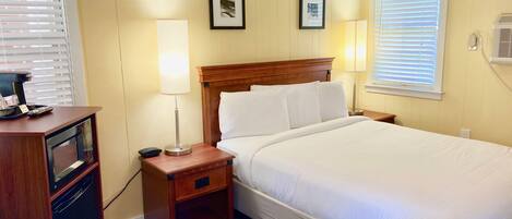 A hotel room with a large bed, bedside tables, a desk with a chair, and a window with blinds.