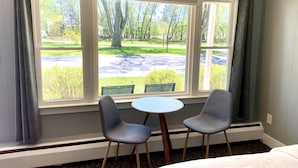A room with a large window, two chairs, a small table, and a bed. - Elk Rapids Lakeshore Inn (Williamsburg)