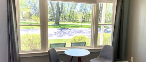 A room with a large window, two chairs, a small table, and a bed.