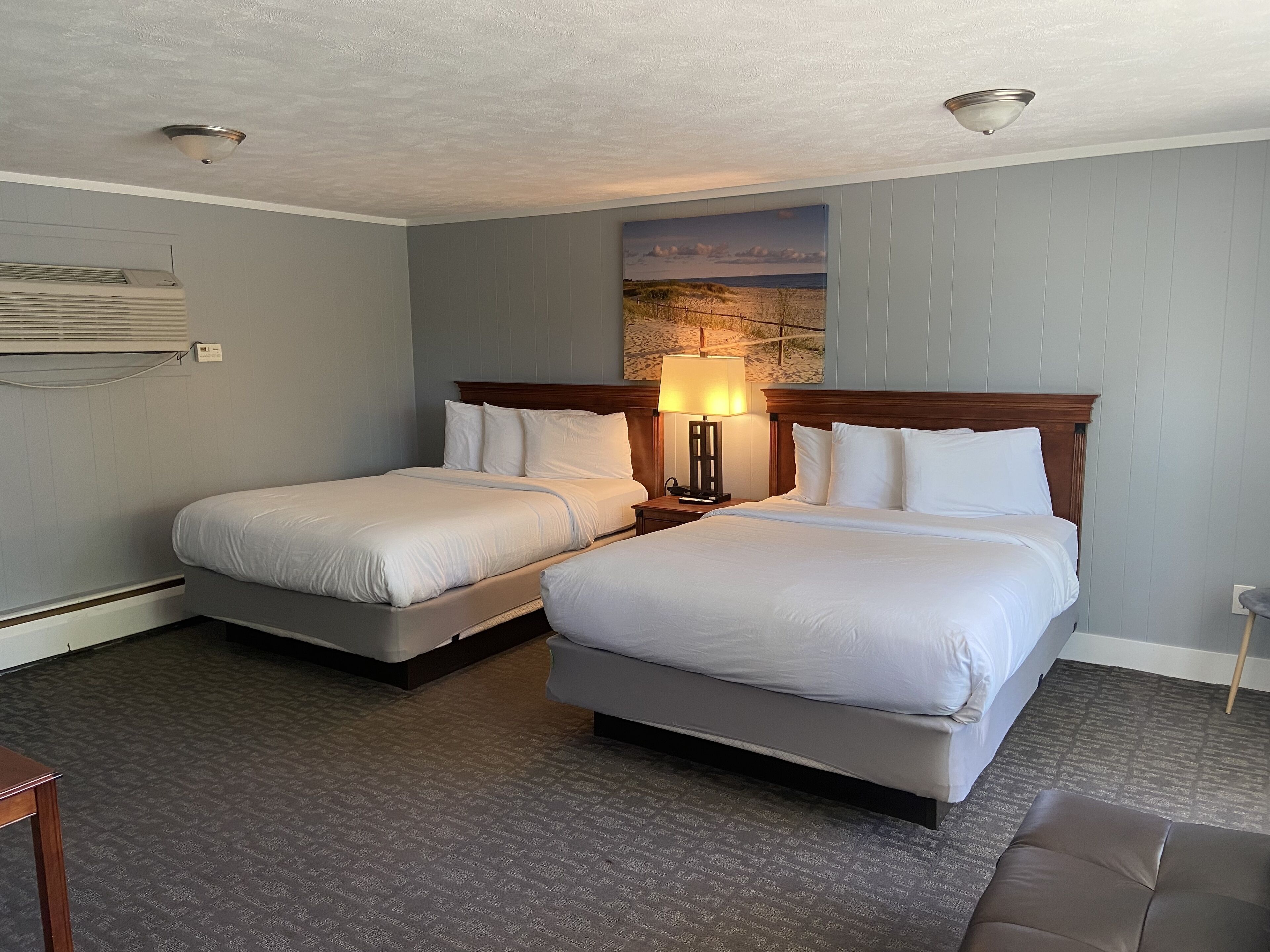 Une chambre d’hôtel avec deux lits, une table de chevet avec une lampe, un tableau au mur et un ventilateur de plafond.