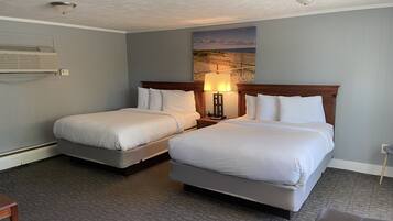 A hotel room with two beds, a nightstand with a lamp, a painting on the wall, and a ceiling fan.