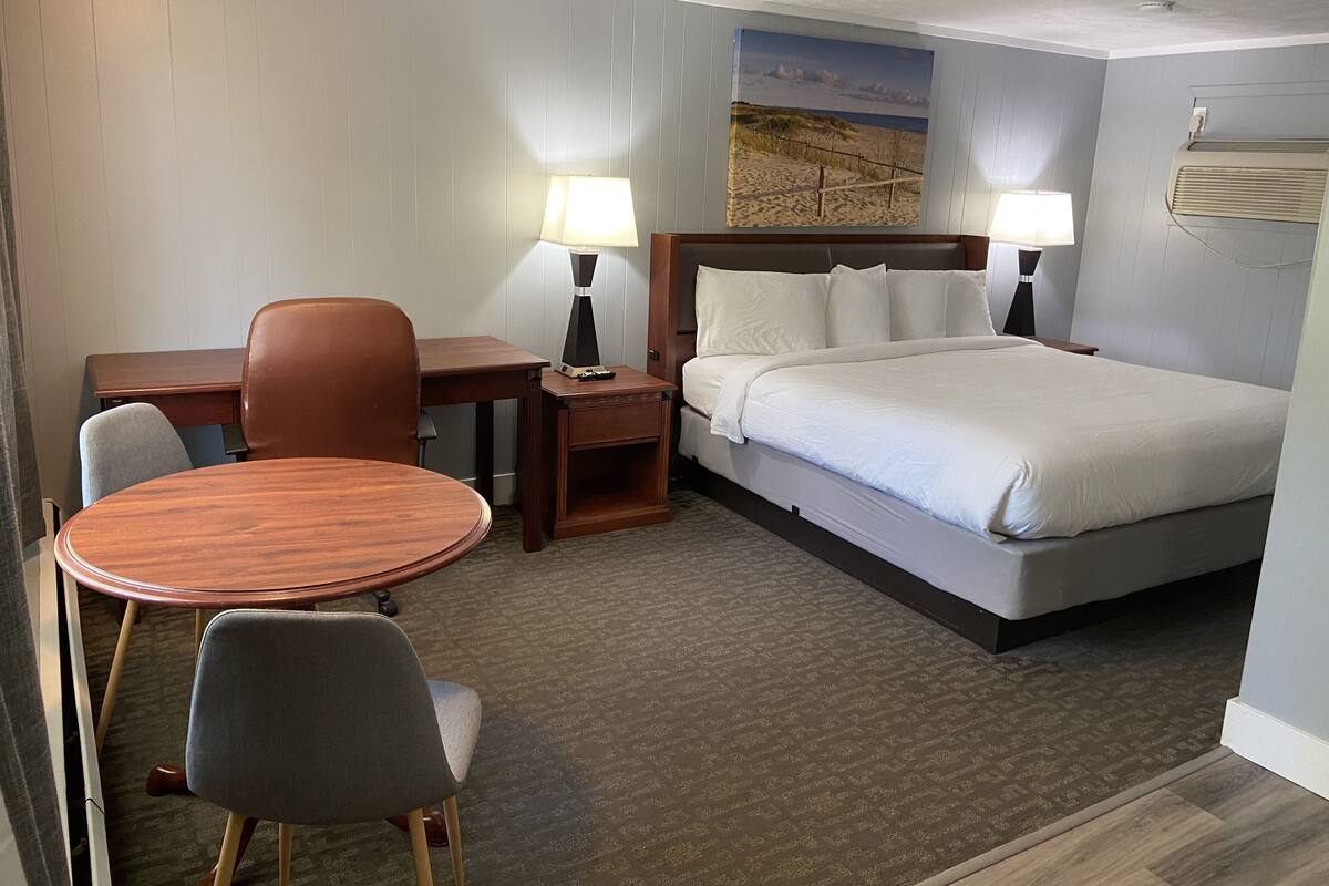 A hotel room with a bed, a desk, a chair, and a small table.