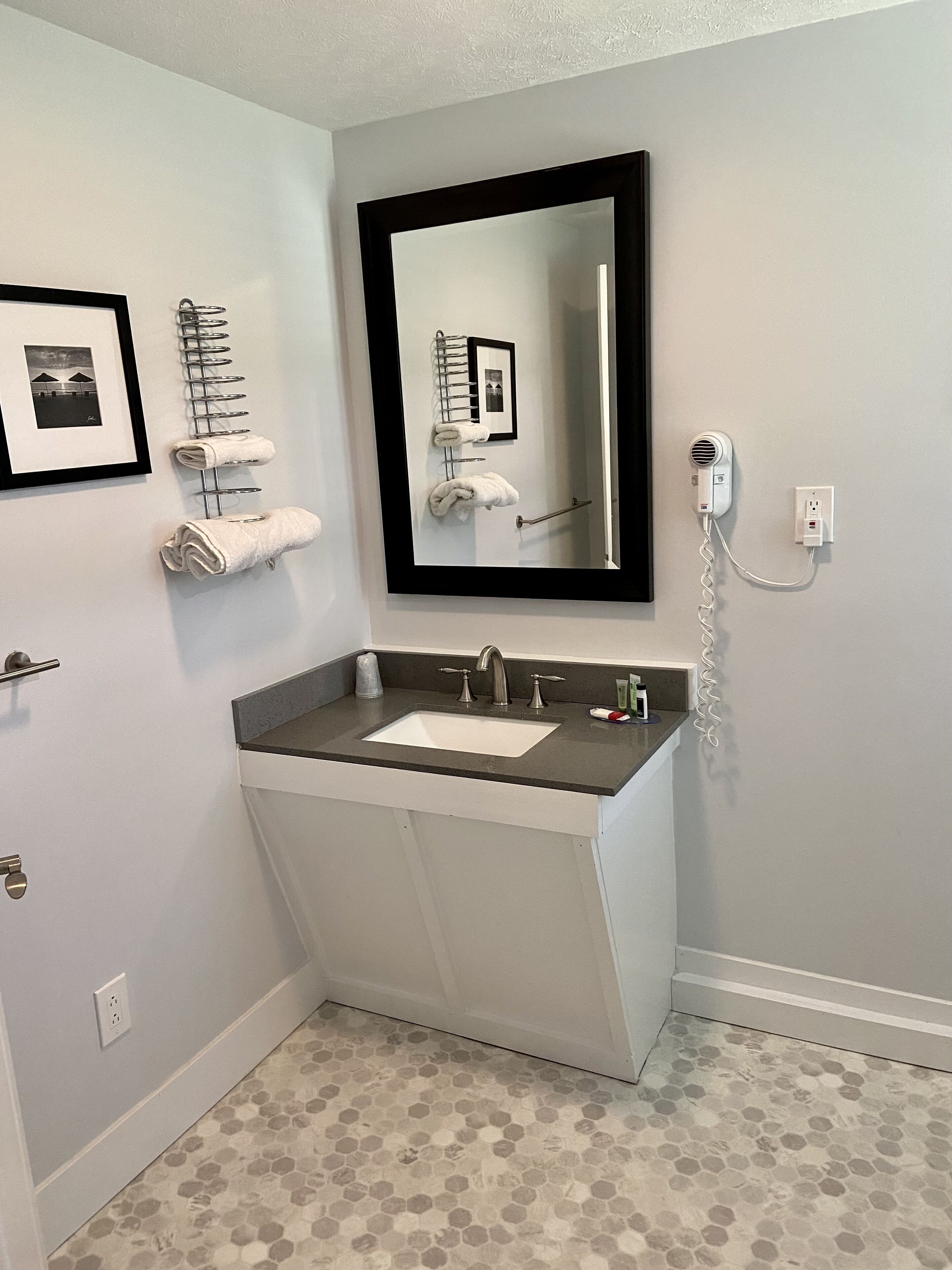 Une salle de bain équipée d’un lavabo, d’un miroir, d’un porte-serviettes et d’un sèche-cheveux.