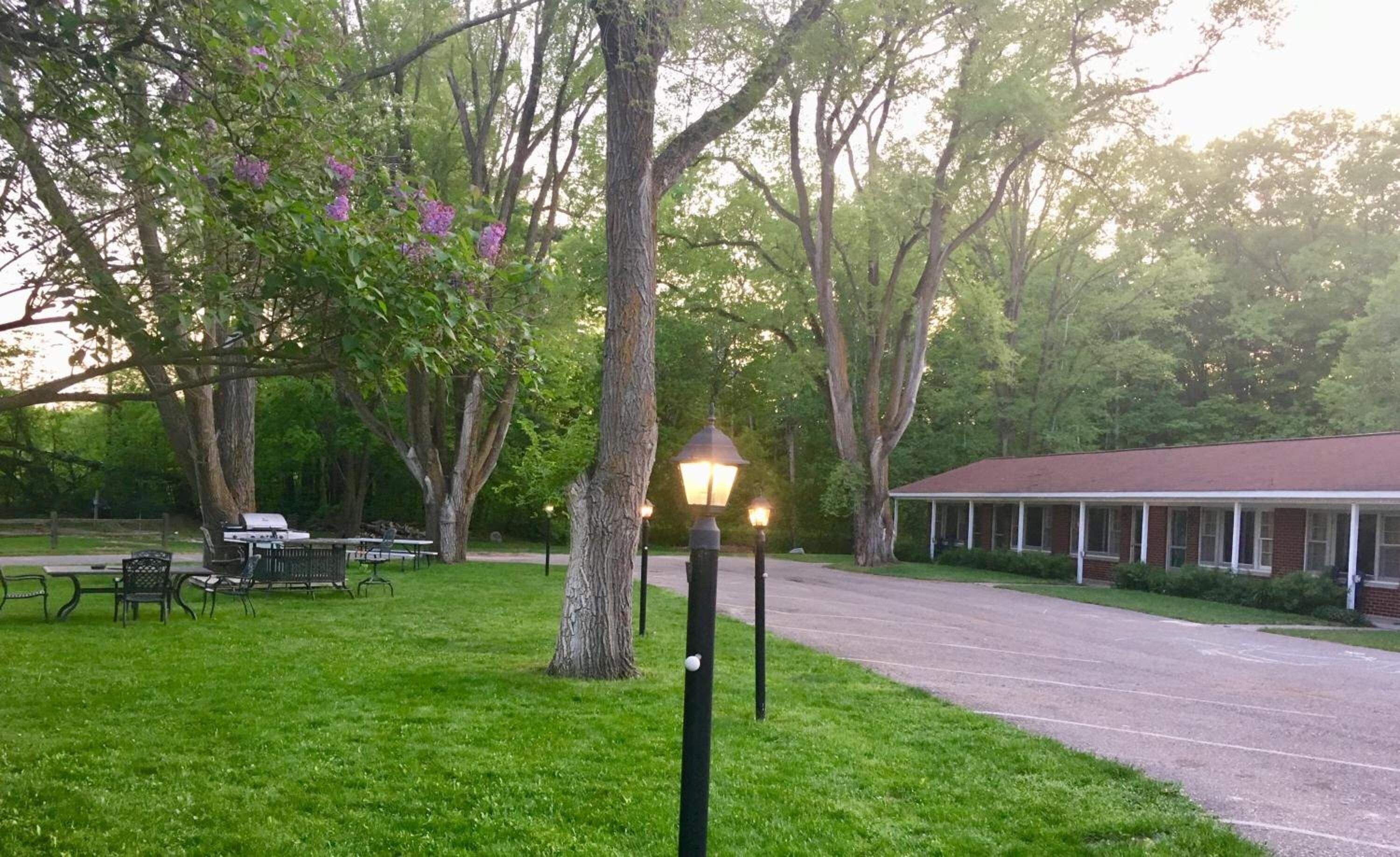 A park with a picnic area, a grill, and a building with a porch.