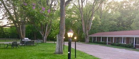 A park with a picnic area, a grill, and a building with a porch.