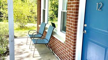 A covered porch with two chairs, a blue door with the number 12, and a brick wall.