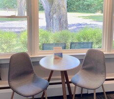 Asiento junto a la ventana con dos sillas y una mesa, con vista a un parque con un árbol grande y un letrero de Lakeshore Inn.