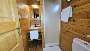 Un baño de cabaña de madera con lavabo, inodoro y espejo sobre el lavabo.