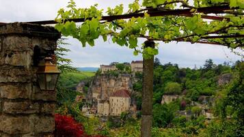A stone building with a lantern, a vine-covered pergola, and a view of a historic village with buildings on a cliff.