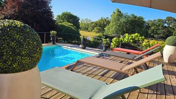 A wooden deck with a swimming pool, lounge chairs, and potted plants.