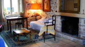A cozy room with a stone wall, a bed, a fireplace, and a table with chairs.