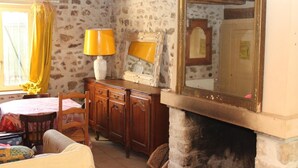 A rustic room with a stone wall, wooden furniture, a fireplace, and a large mirror.
