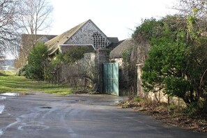 Un camino rural que lleva a un edificio de piedra con techo de tejas y una verja verde.
