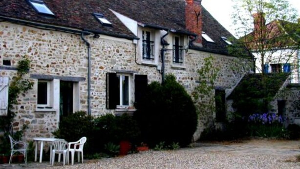 A stone building with a sloped roof, a chimney, and a gravel courtyard with white chairs.