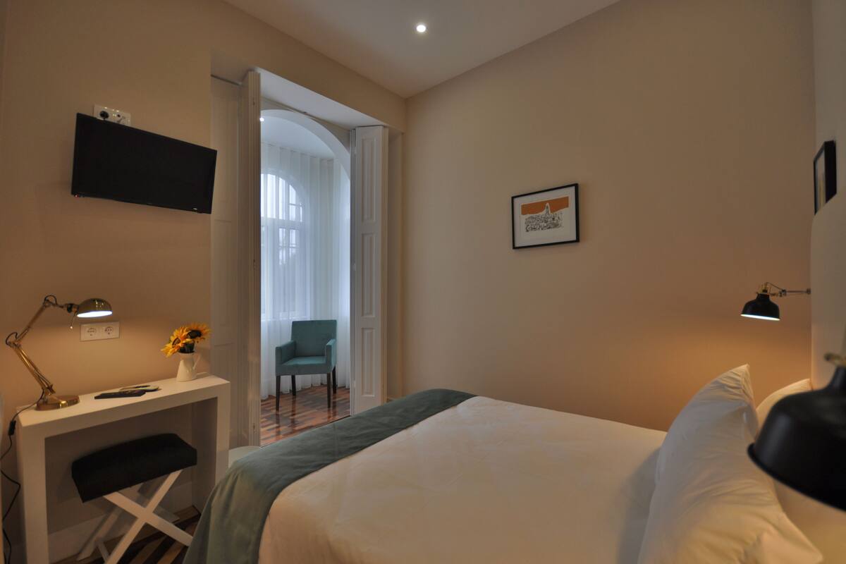Habitación de hotel con cama, escritorio, silla y televisor montado en la pared.
