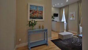 A modern living room with a blue console table, a painting of a European town, a small white ottoman, and a TV mounted on the wall. - Porto Charming Hotel (Porto)