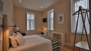 A hotel room with two beds, a desk, a chair, and a TV on the wall. - Porto Charming Hotel (Porto)