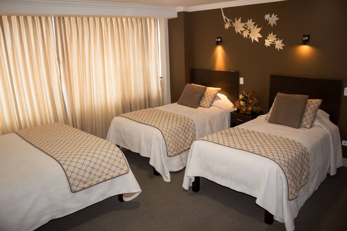 Ein Hotelzimmer mit zwei Betten, einem großen Fenster mit Vorhängen und einer Wandleuchte.