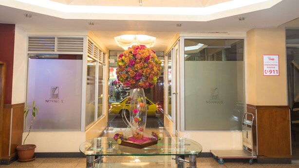 A reception area with a glass table, a chandelier, and a floral arrangement. - Hotel Novalux (Ambato)
