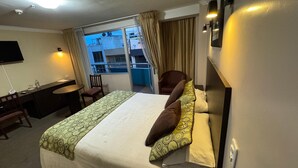 A hotel room with a bed, a desk, a chair, a TV, and a balcony with a view. - Hotel Novalux (Ambato)
