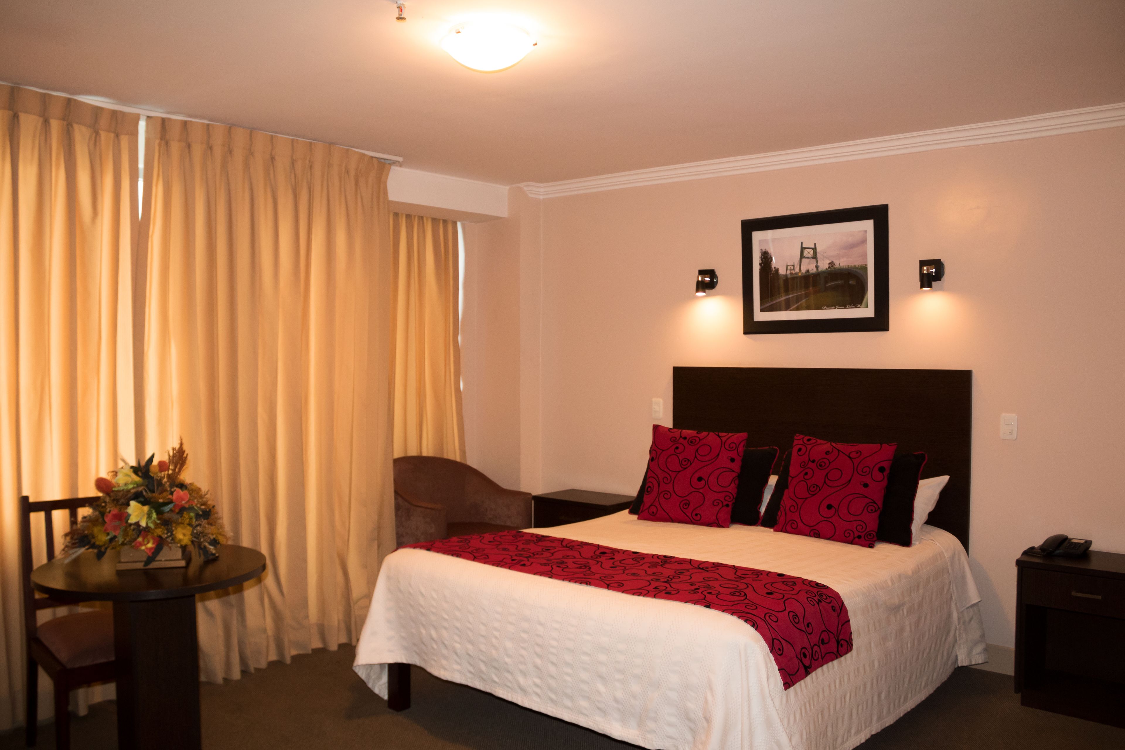 Een hotelkamer met een bed, een stoel, een tafel met bloemen en een lijst met een afbeelding aan de muur.