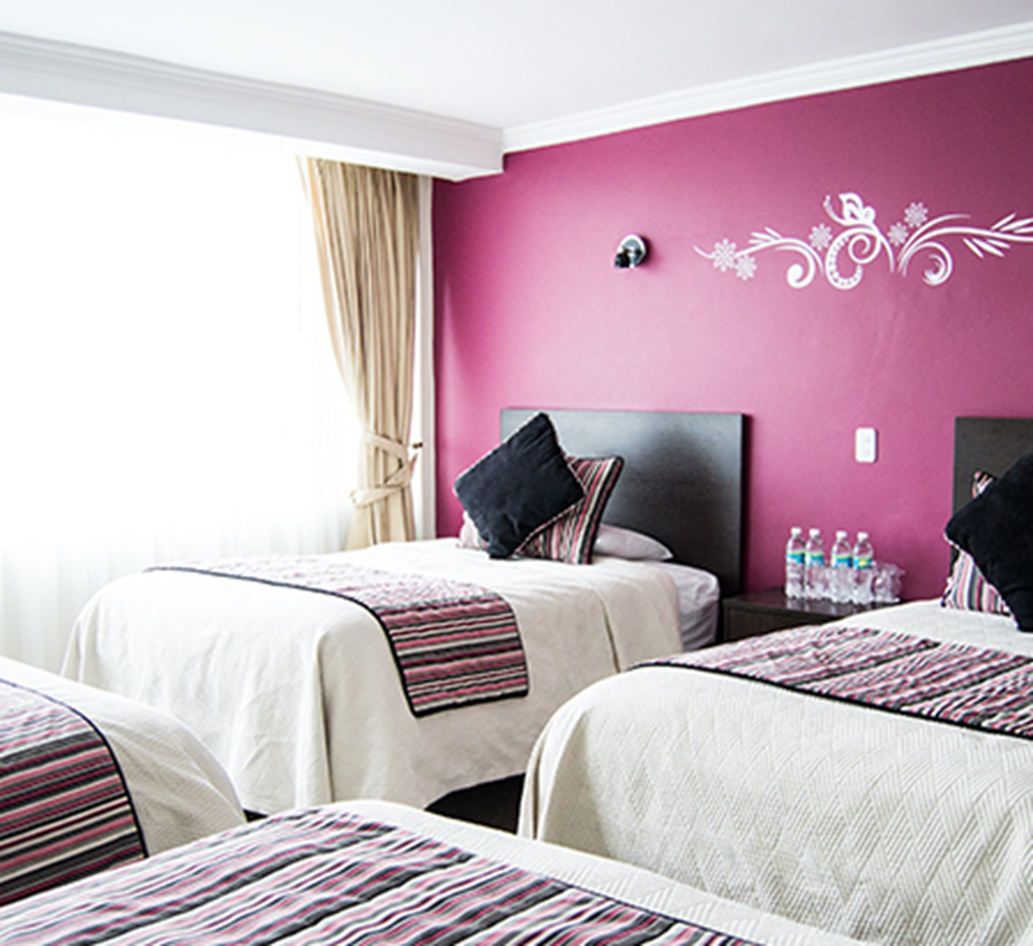 A hotel room with two beds, a pink wall, and a window with curtains.