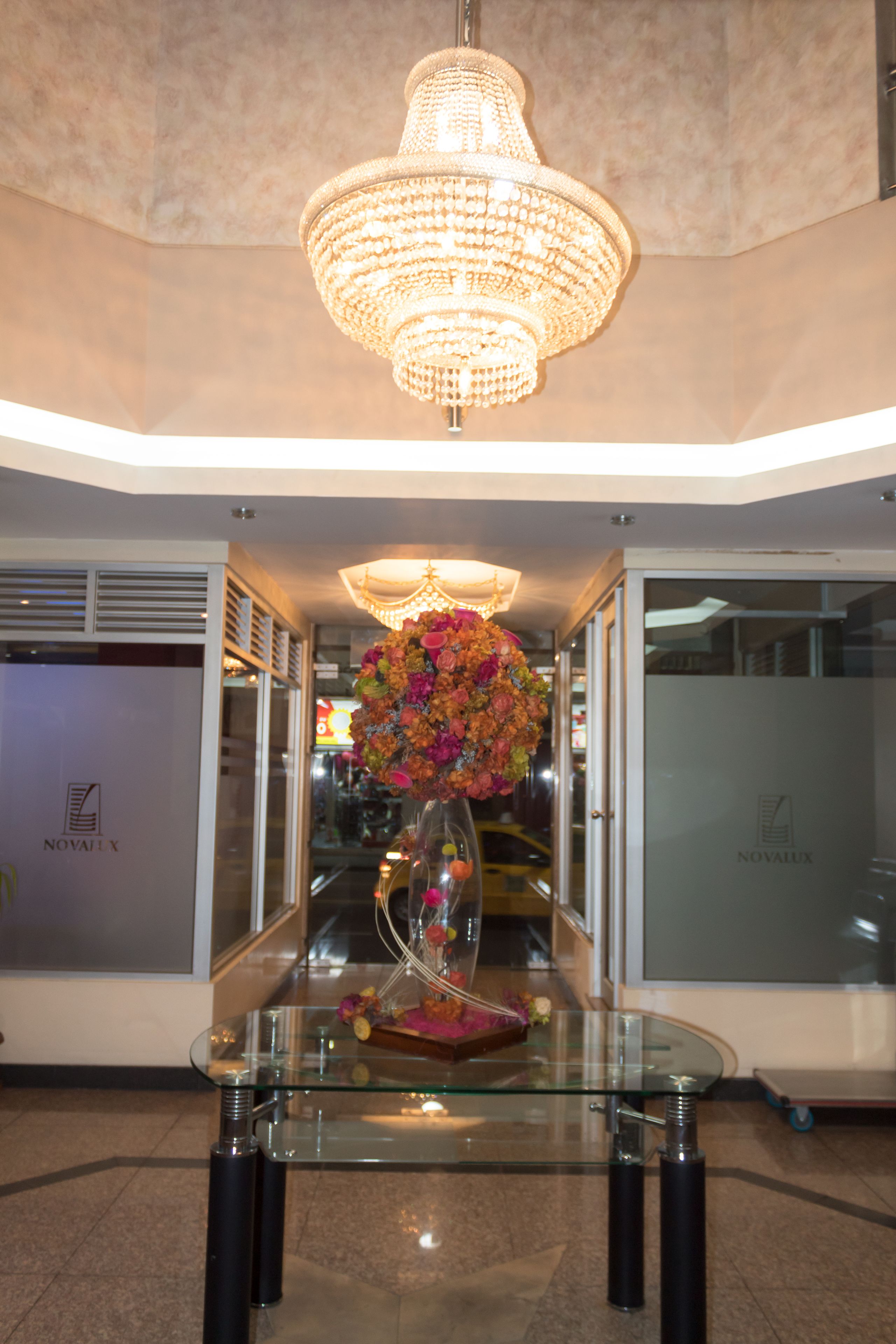 A lobby with a glass table, a chandelier, and a floral arrangement.