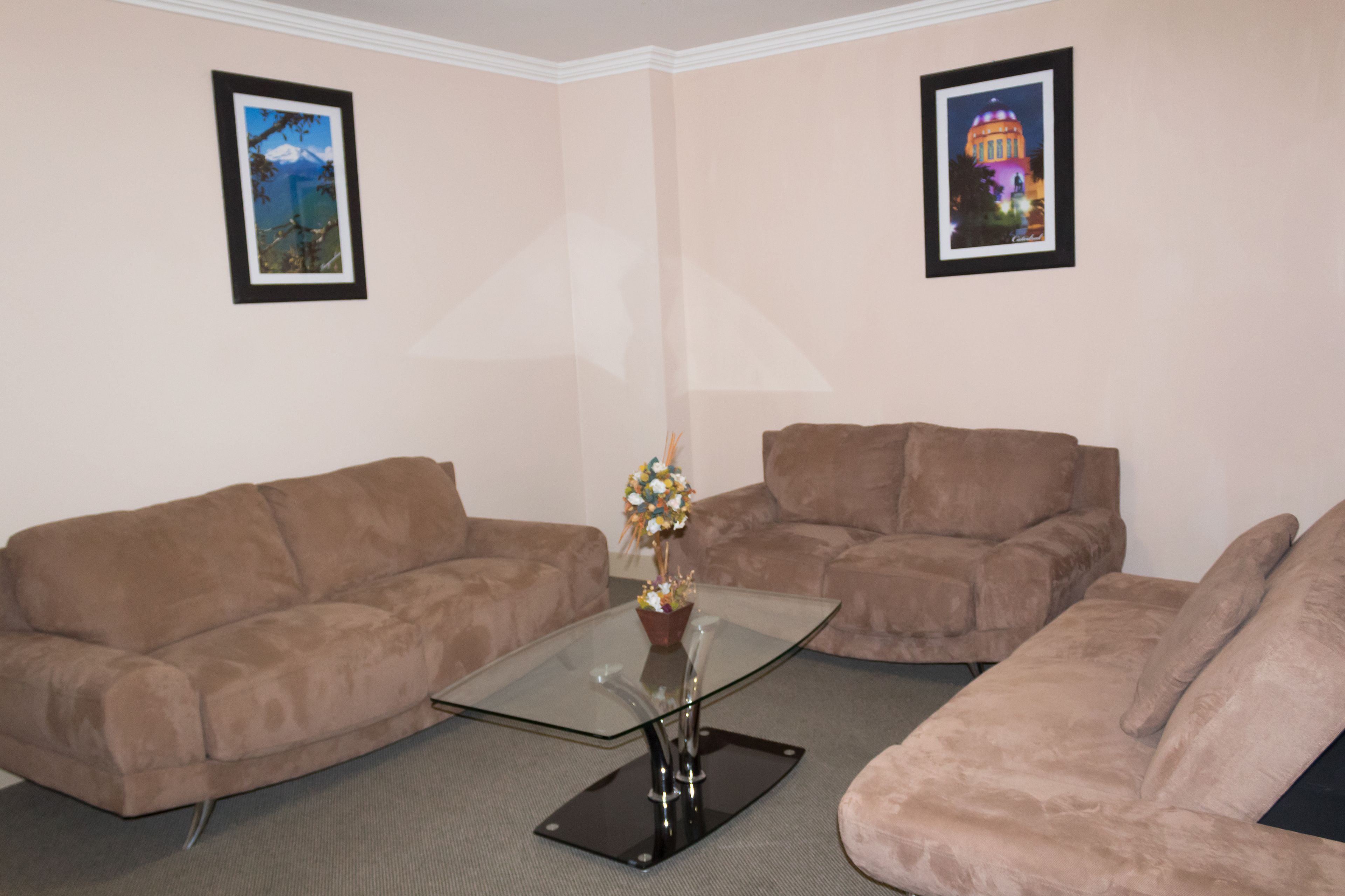 A living room with two brown sofas, a glass coffee table, and two framed pictures on the walls.