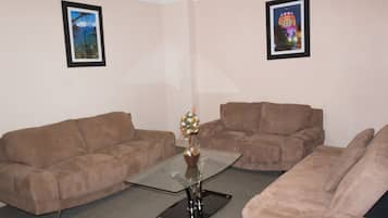 A living room with two brown sofas, a glass coffee table, and two framed pictures on the walls.