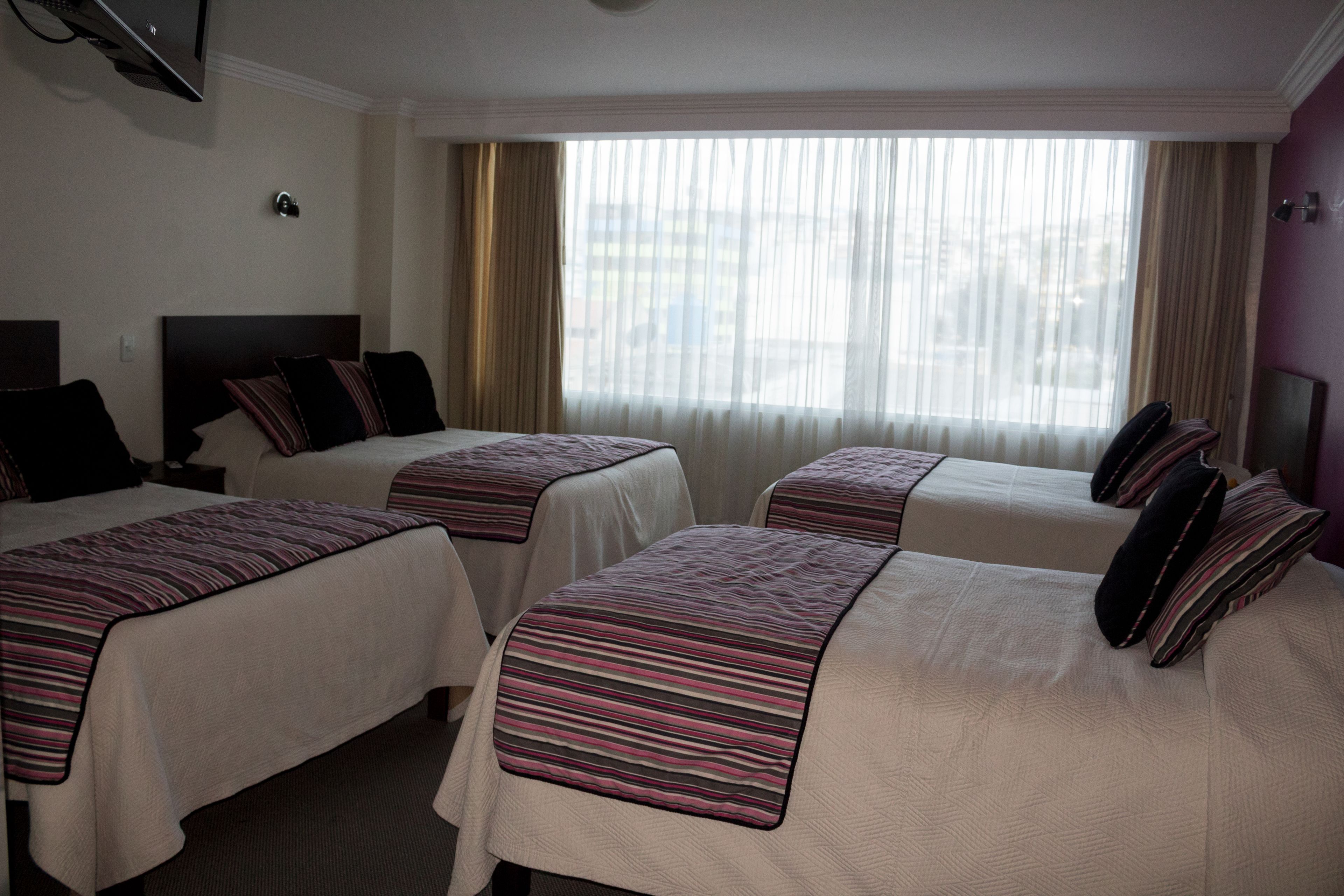 Ein Hotelzimmer mit drei Betten, jeweils mit gestreifter Bettdecke und Kissen.
