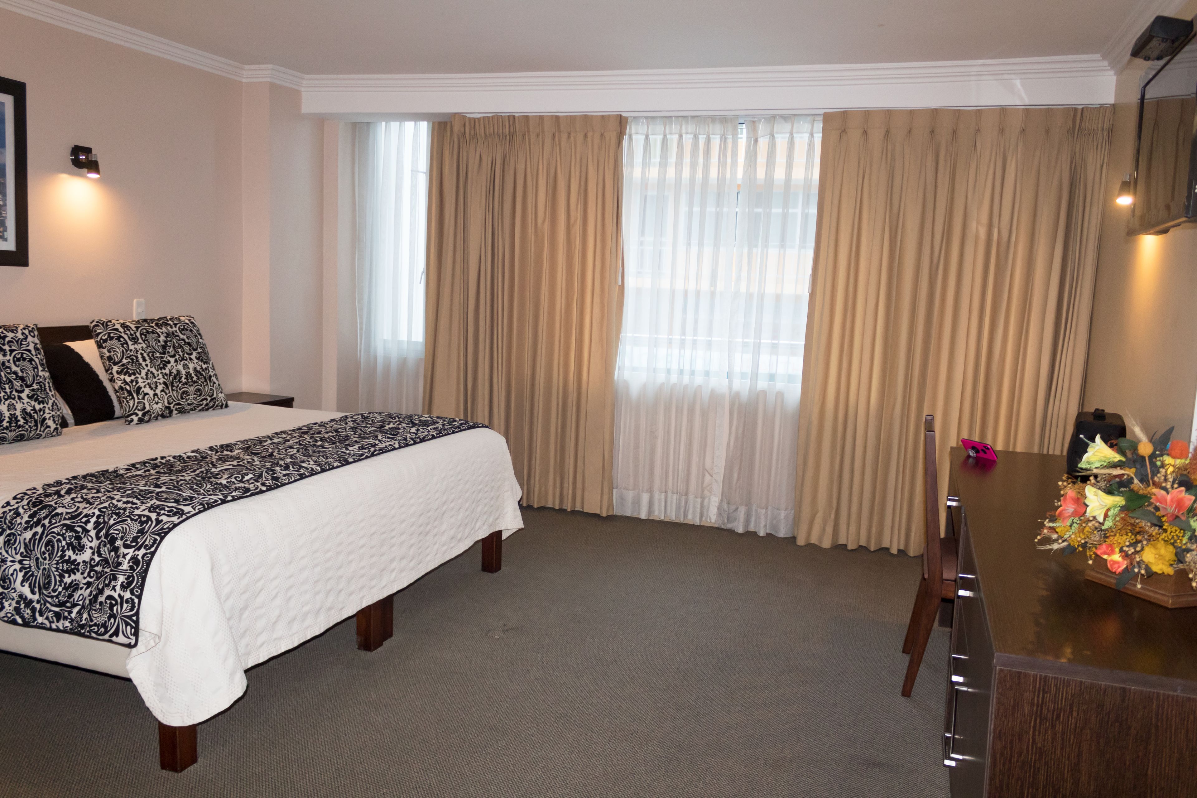 A hotel room with a large bed, a desk with a vase of flowers, and a window with curtains.