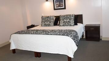 Un lit bien fait, avec une couvre-lit à motifs et des oreillers, une table de chevet avec une lampe, et un tableau encadré accroché au mur.
