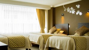 A hotel room with two beds, a large window with curtains, and a wall-mounted light fixture. - Hotel Novalux (Ambato)