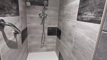 A shower area with a handheld showerhead, a wall-mounted faucet, and a rectangular drain.
