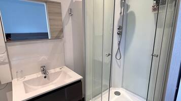 Un bagno moderno con cabina doccia in vetro, lavabo con specchio sopra e mobile contenitore scuro.