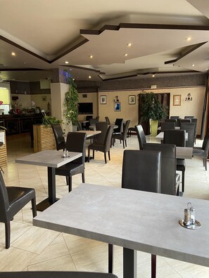A modern restaurant with a clean, minimalist design, featuring a mix of table and booth seating, a flat-screen TV, and a variety of wall art. - Hôtel L'Univers (Chatellerault)