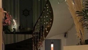 A spiral staircase with string lights, a wooden floor, and a door in the background. - Hôtel L'Univers (Chatellerault)