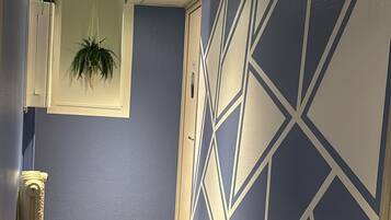 A hallway with a geometric patterned wall, a potted plant, and a textured carpet.
