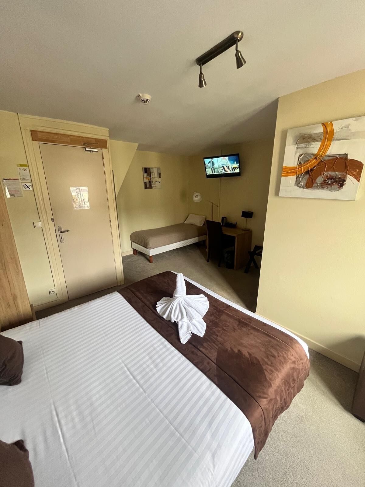 A hotel room with a large bed, a desk, a television, and a door with a security camera.
