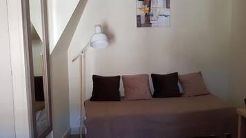 Een kleine, eenvoudig ingerichte kamer met een enkel bed, een staande vloerlamp en een aan de muur hangend schilderij.