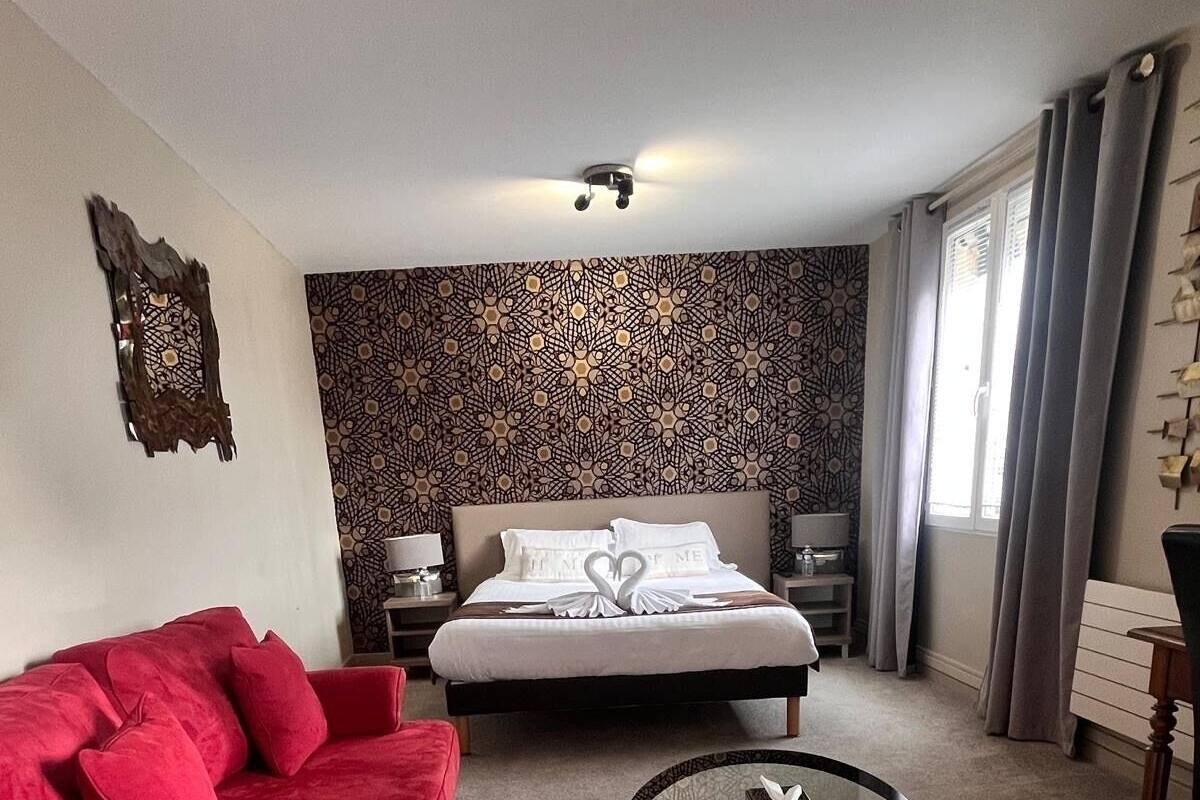 A hotel room with a red sofa, a round glass coffee table, a bed with a heart-shaped decoration, and patterned wallpaper.