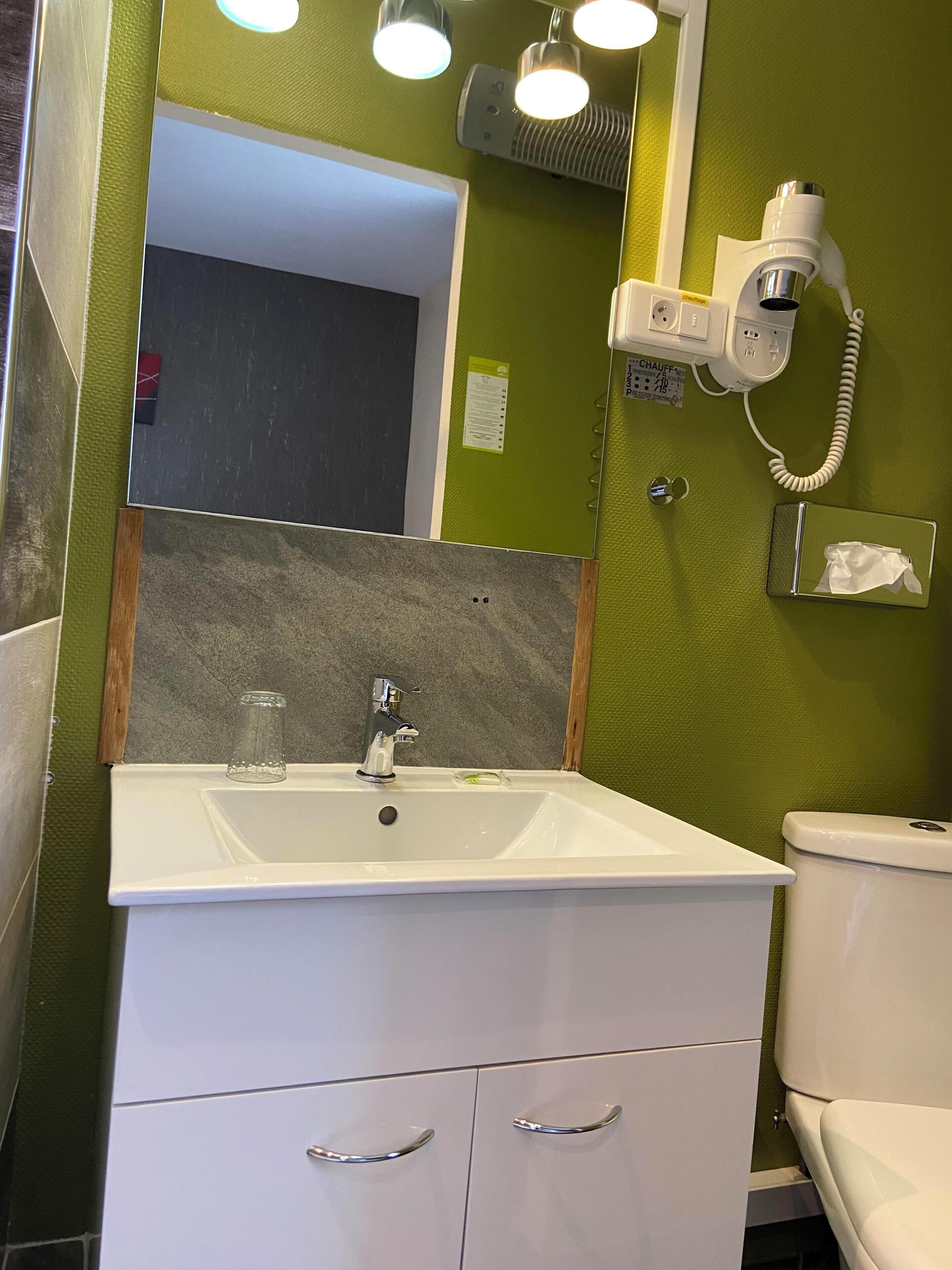 A bathroom with a white sink, a mirror, a towel dispenser, and a toilet.