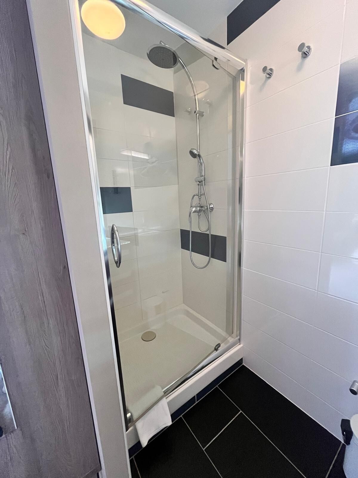 A glass-enclosed shower stall with a handheld showerhead and a wall-mounted faucet.