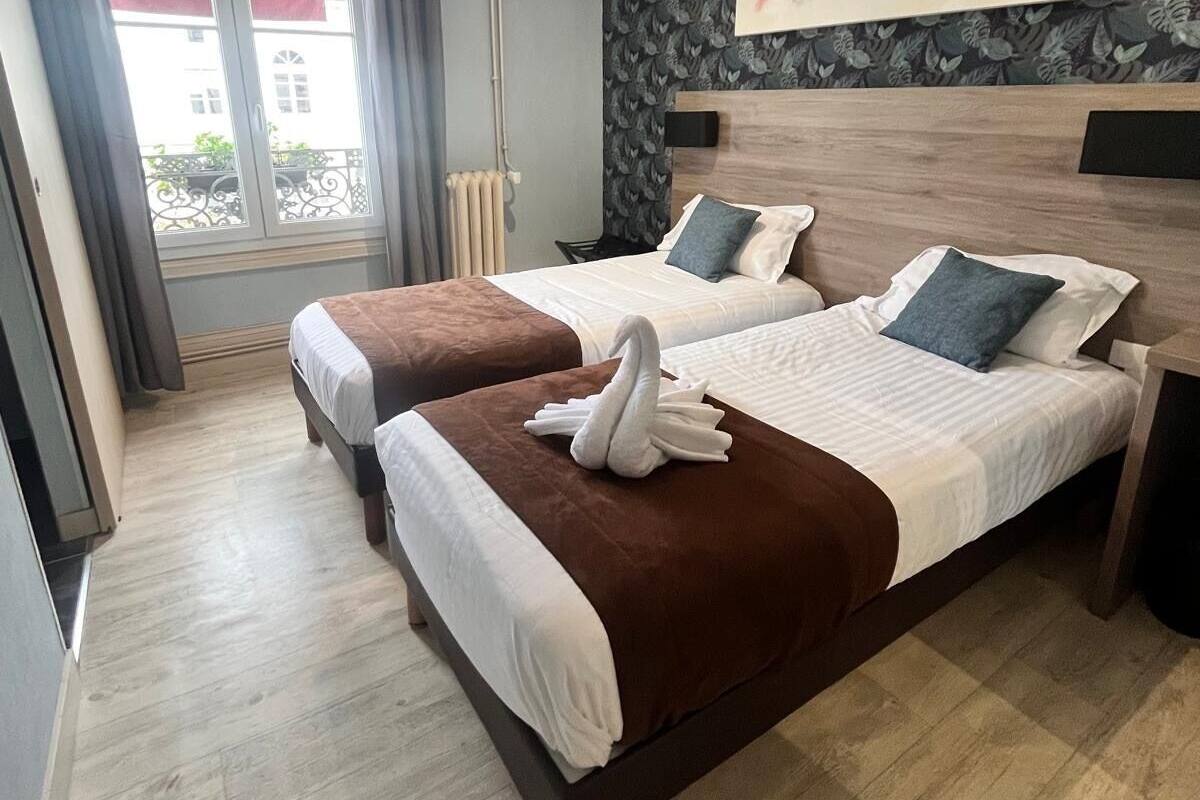 A hotel room with two beds, a large window with curtains, a radiator, and a wall-mounted artwork.