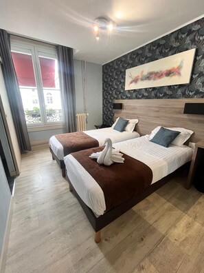 A hotel room with two beds, a large window with curtains, a radiator, and a wall-mounted artwork. - Hôtel L'Univers (Chatellerault)