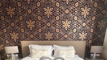 Habitación de hotel con una cama grande, dos almohadas bordadas con la palabra 'HOME' y una mesita de noche con lámpara, además de un motivo decorativo en la pared.