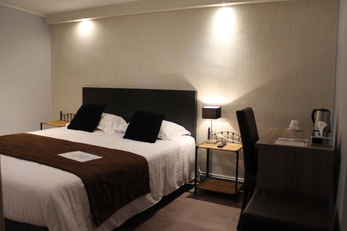 A hotel room with a bed, bedside tables, a desk, and a chair.